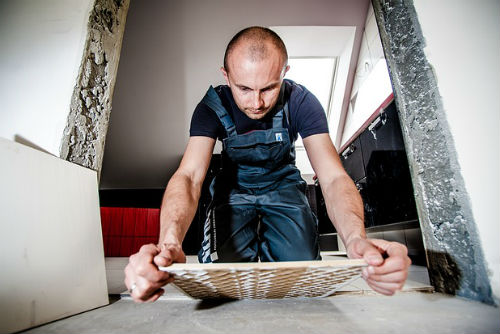 A man wearing overalls laying tiles in a bathroom