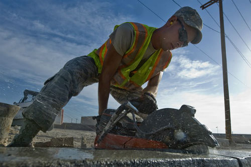 A man in a construction vest using a concrete saw on a sidewalk in Columbus