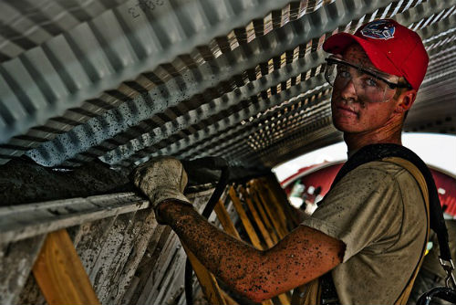 A young man in a hat and gloves working in an attic space