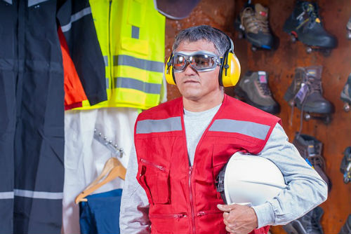 A man wearing noise cancelling headphone and holding a hard hat