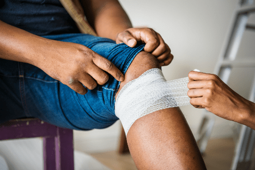 A person having their knee wrapped in an ace bandage.