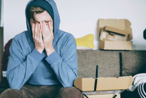 A young man in a hooded sweatshirt holding his face in his hands.