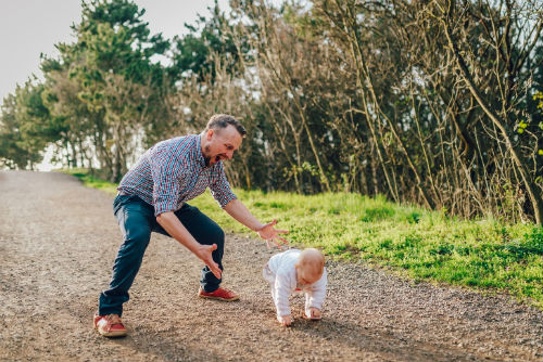 A man getting excited while following closely behind his newly walking child.