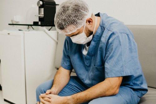 A man in scrubs sitting in a chair hanging his head.