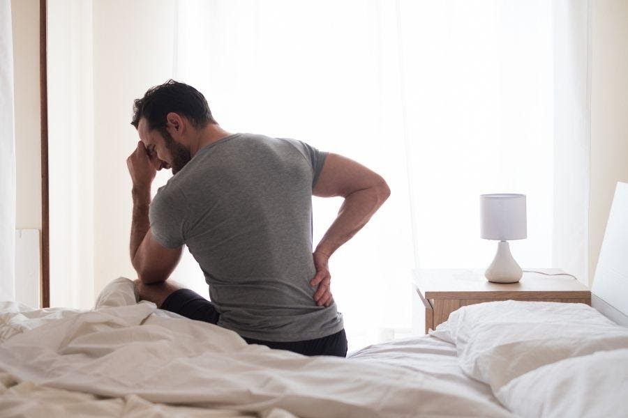 A man getting out of bed and holding his back in pain from a work injury