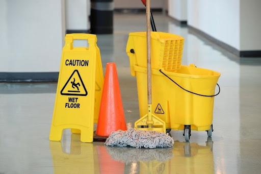 A sign that reads "Caution, Wet Floor" in a hallway next to a bucket and mop.