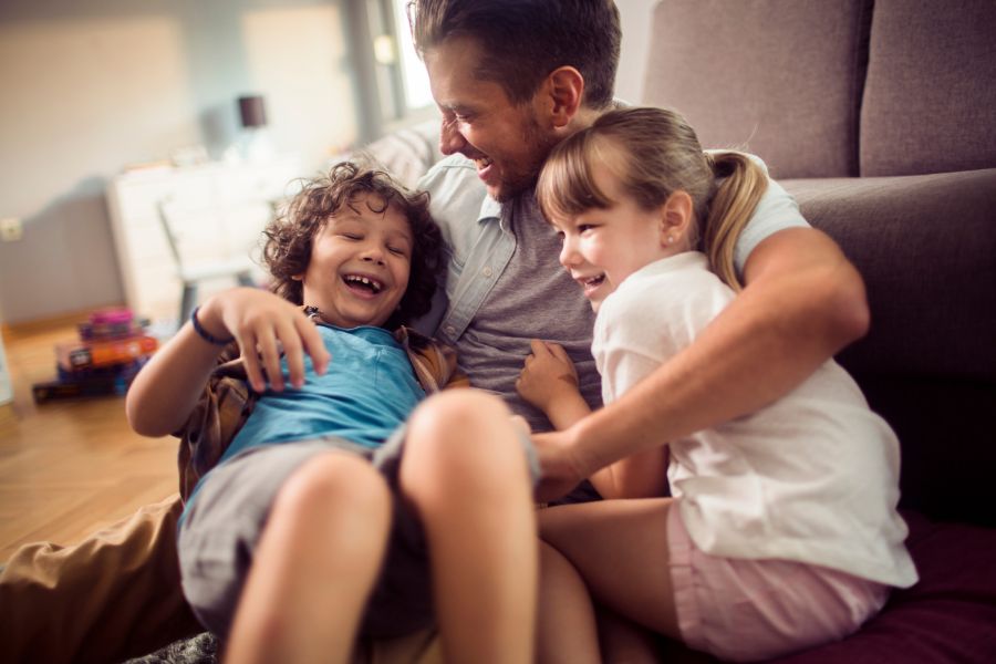 A father laughing and playing with his son and daughter